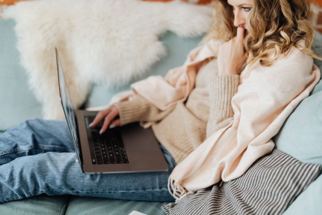 Person in a soft cream cardigan typing on a laptop on a cozy sofa