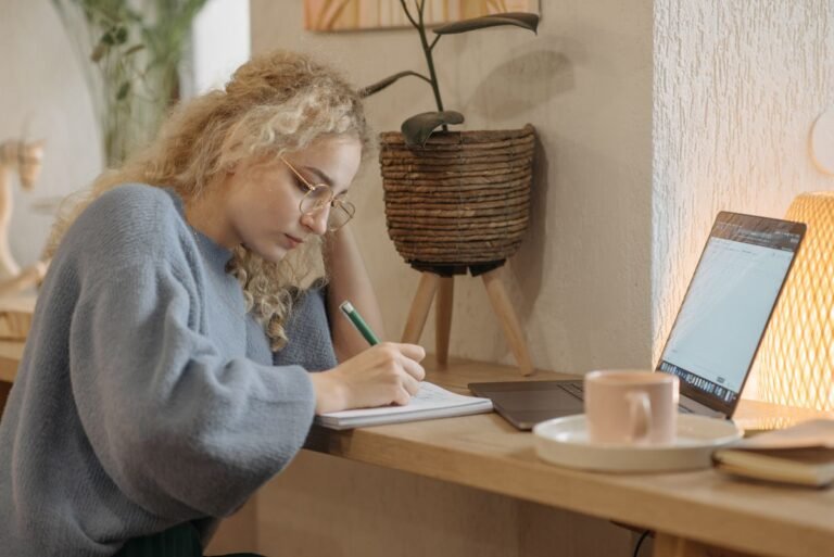 Woman writing in a notebook beside a laptop