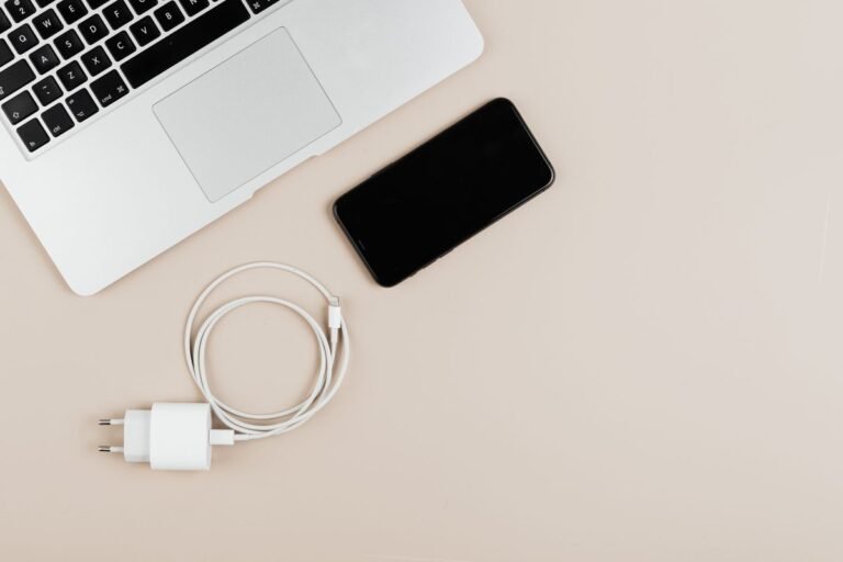 Laptop, smartphone and charging cable on a beige surface